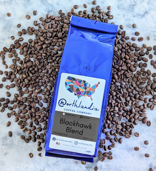Blue coffee bag labeled 'Blackhawk Blend' from Northlandia Coffee Company on a bed of coffee beans.
